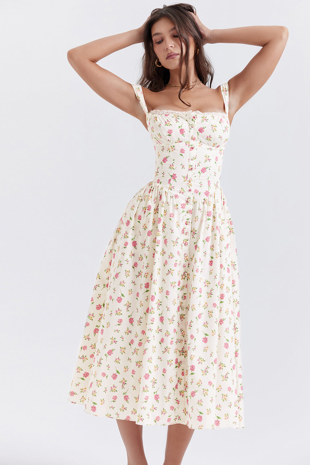 Robe longue à fleurs roses et jaunes sur fond blanc, bretelles fines, style vintage, portée par une femme posant avec les bras levés.