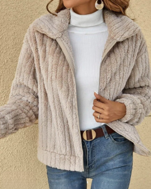 Femme portant une veste en fausse fourrure beige, col roulé blanc, jeans bleu, boucle de ceinture marron, boucles d'oreilles pendantes. Mode automne-hiver.