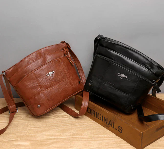 Deux sacs à bandoulière en cuir, marron et noir, posés sur une boîte en bois. Design élégant avec logo animal, parfait pour mode et accessoires.