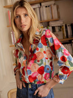 Femme portant une chemise à motifs floraux colorés, debout devant une bibliothèque. Mode féminine, style décontracté, chemise imprimée tendance.