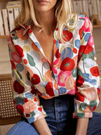 Femme portant une chemise à motifs floraux colorés, assise devant une étagère. Mode féminine, style décontracté, chemise imprimée tendance.