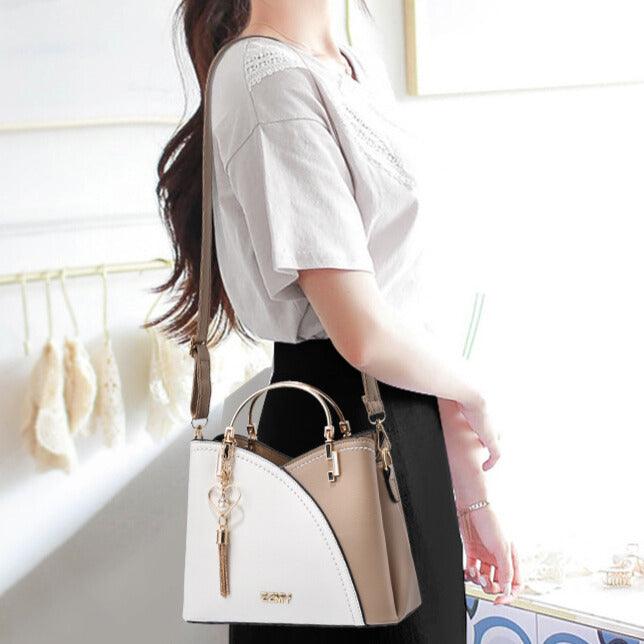Femme portant un sac à main en cuir bicolore blanc et beige, design élégant avec breloque dorée, mode féminine chic et tendance.