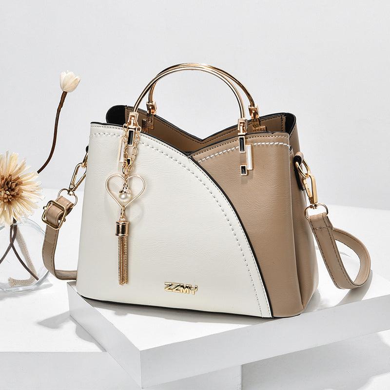 Sac à main en cuir bicolore beige et blanc avec poignée dorée, pendentif cœur, design élégant. Accessoire mode femme tendance.