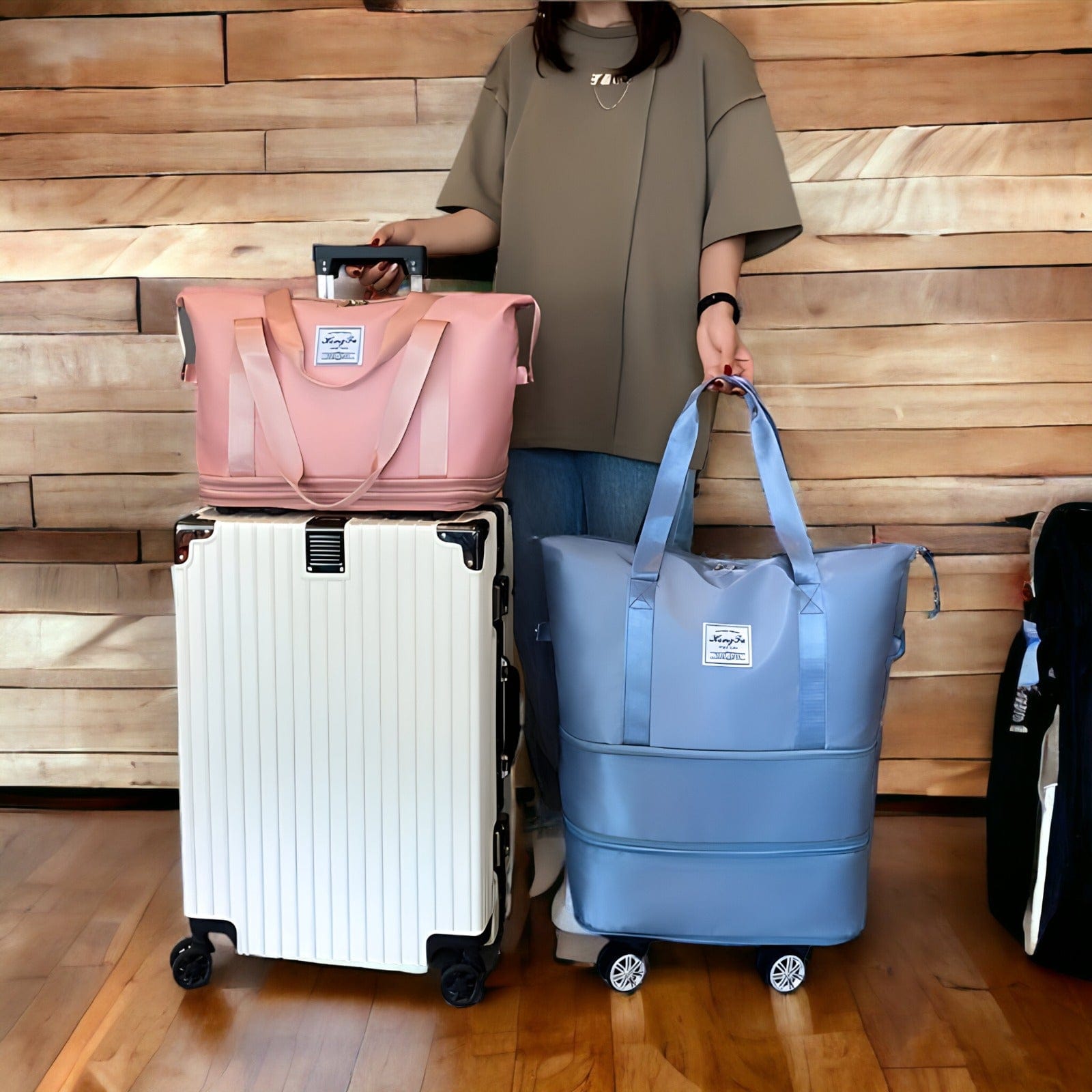 Femme avec valise blanche et sacs de voyage rose et bleu sur roulettes, posés sur un sol en bois devant un mur en bois. Accessoires de voyage modernes.
