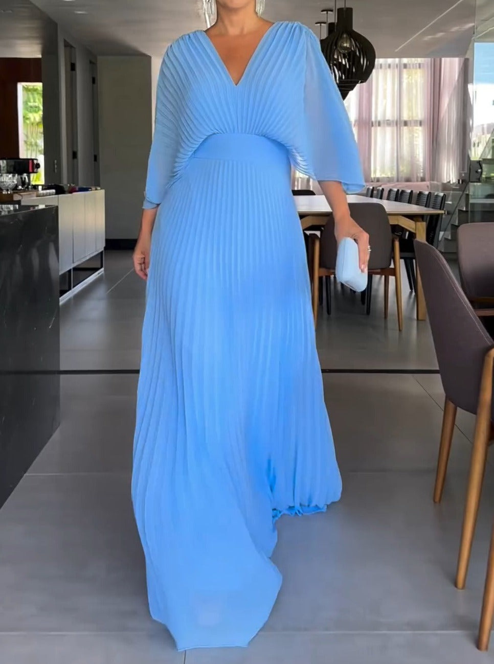 Robe longue plissée bleue élégante, manches évasées, portée par une femme dans un intérieur moderne. Mode féminine chic, tenue de soirée.