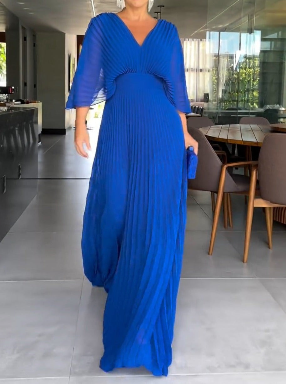Robe longue plissée bleue élégante portée par une femme, intérieur moderne en arrière-plan, style chic et sophistiqué, mode féminine tendance.