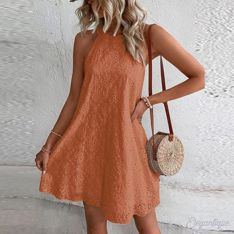 Robe d'été orange en dentelle portée par une femme blonde, accessoirisée d'un sac rond en osier et d'un chapeau. Mode féminine estivale tendance.