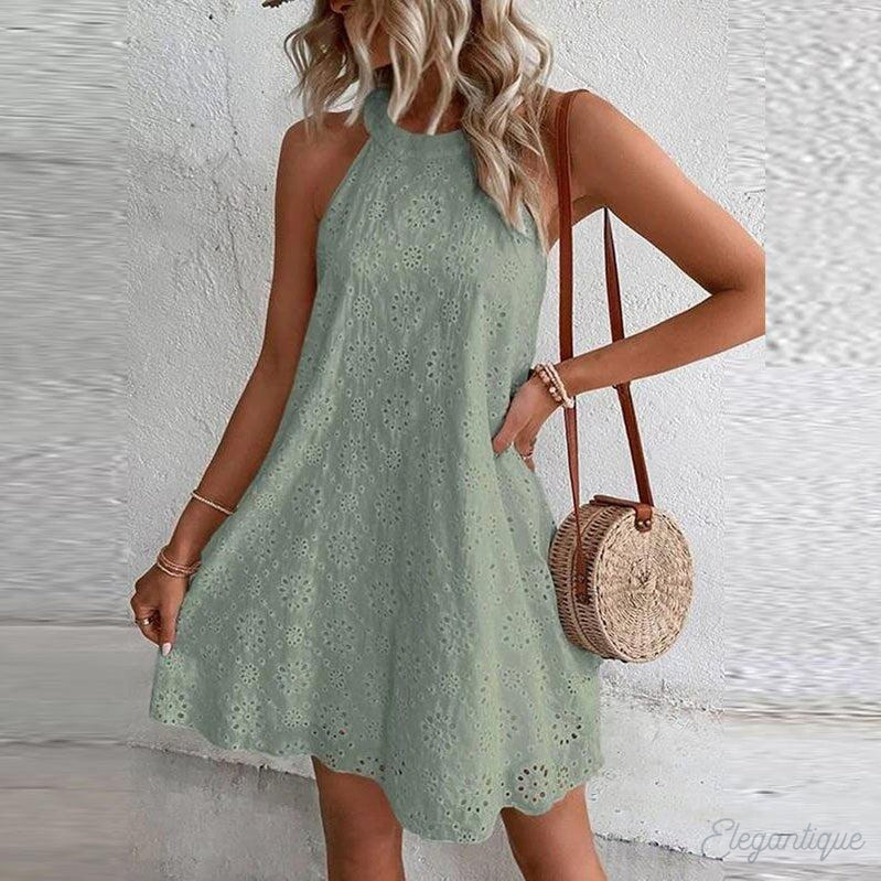 Robe d'été verte en dentelle brodée, sans manches, portée par une femme blonde avec sac rond en osier. Mode féminine chic et décontractée.
