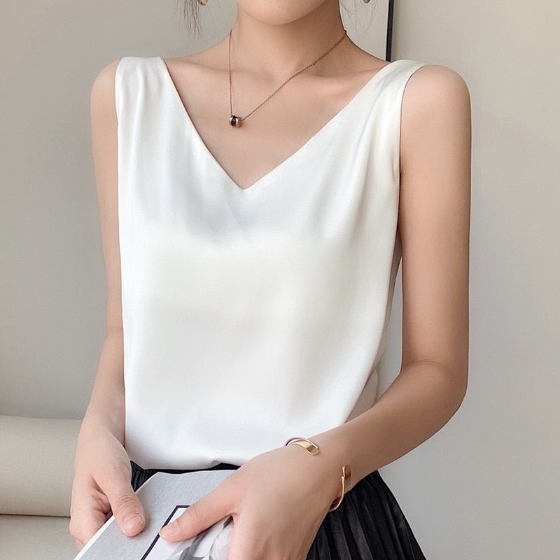 Femme portant un débardeur blanc élégant avec un col en V, collier discret, jupe noire plissée. Mode féminine chic et minimaliste.