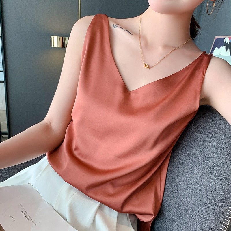 Débardeur en satin rose porté par une femme assise, avec un collier délicat. Mode féminine élégante, tenue estivale chic, style décontracté.