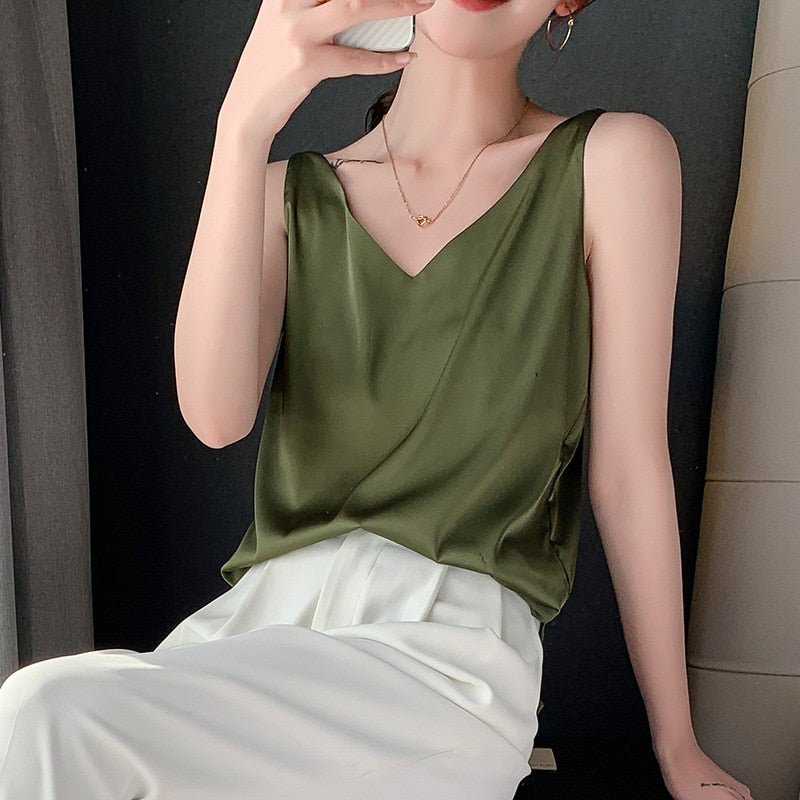 Femme portant un débardeur vert en satin avec un pantalon blanc, tenant un smartphone. Mode élégante, tenue chic, style décontracté.