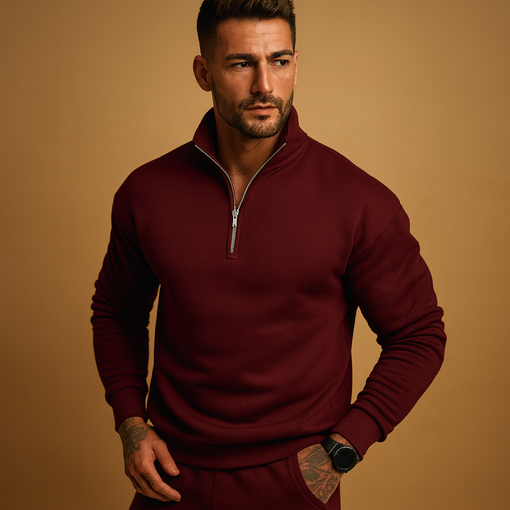 Homme portant un pull bordeaux à col zippé, posant sur fond beige. Mode masculine élégante, tenue automne-hiver, style décontracté chic.