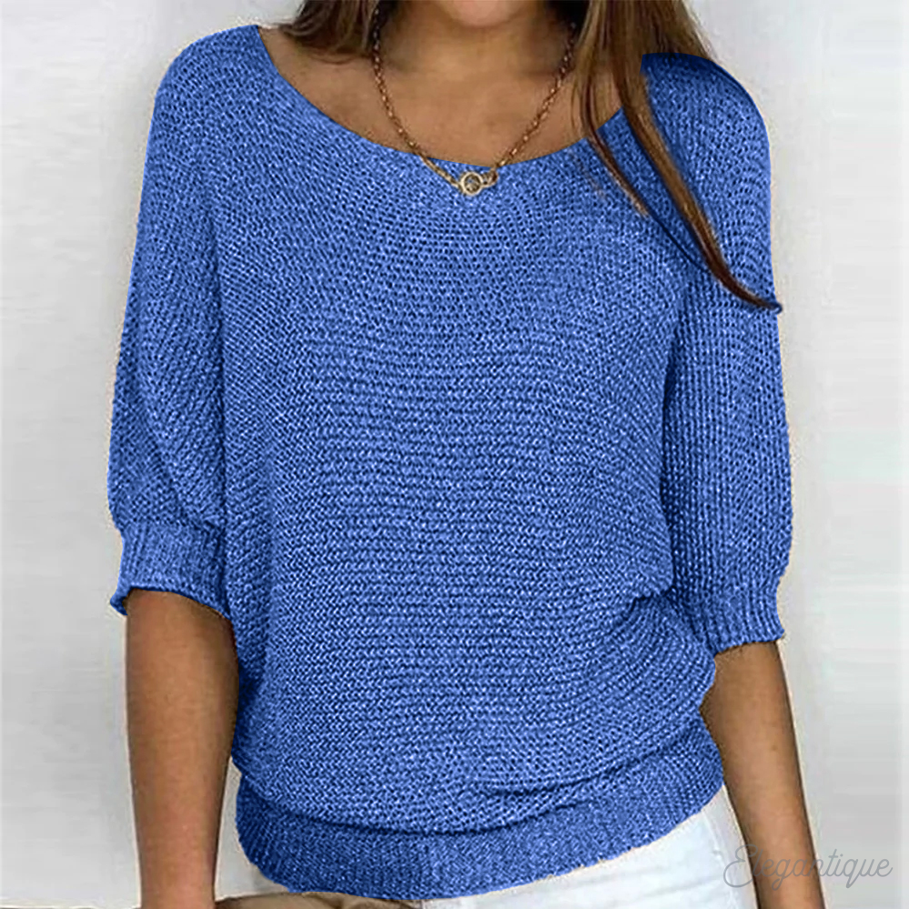 Femme portant un pull bleu en tricot, manches trois-quarts, col bateau, avec un collier doré. Mode féminine, tenue décontractée élégante.