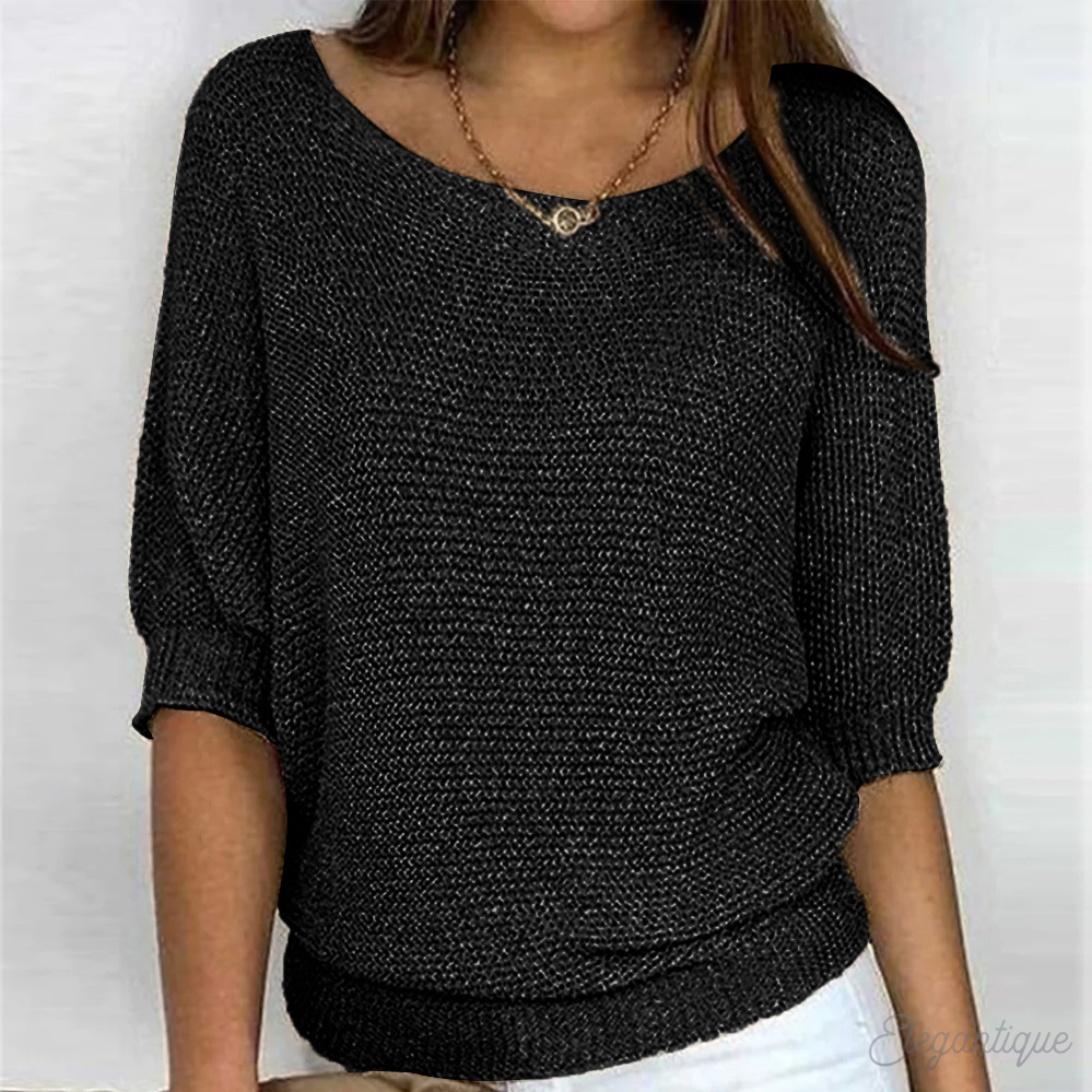 Femme portant un pull noir à manches trois-quarts, col bateau, texture tricotée, avec un collier doré. Mode féminine élégante et décontractée.