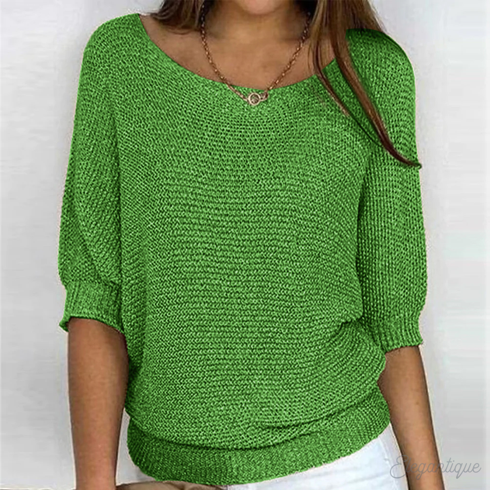 Femme portant un pull vert en tricot, manches trois-quarts, col bateau, avec un collier doré. Mode féminine, tenue décontractée, style élégant.