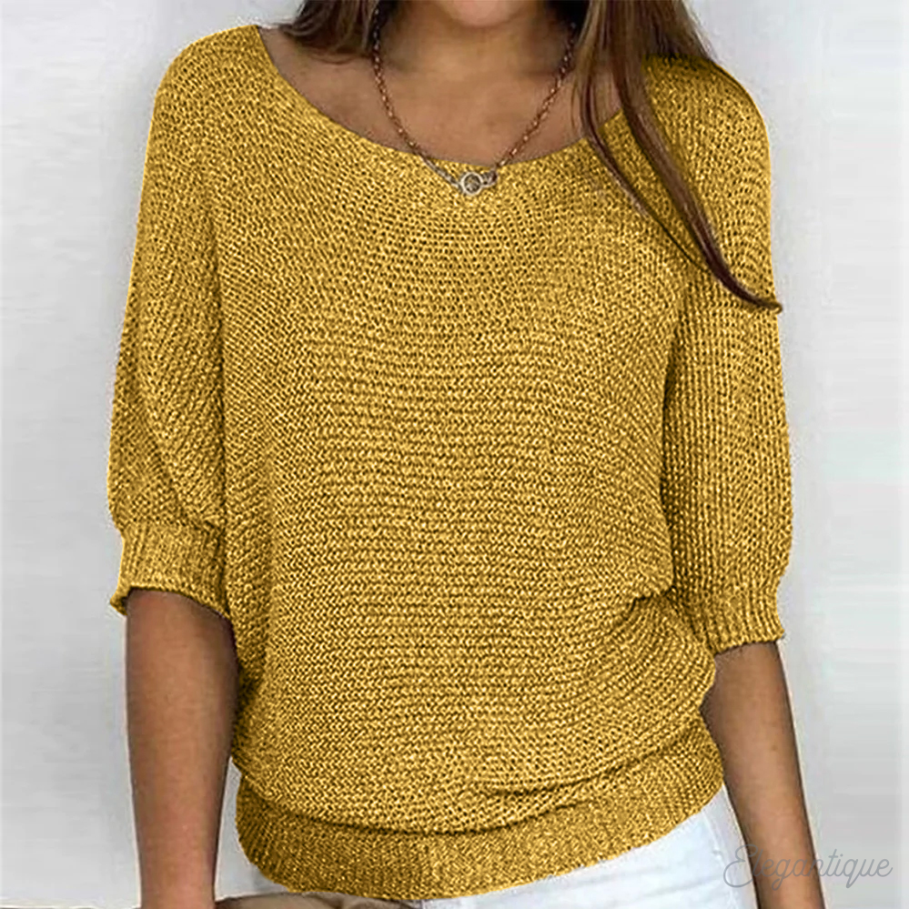 Femme portant un pull jaune en tricot, manches trois-quarts, col bateau, avec un collier discret, sur fond blanc. Mode automne-hiver tendance.