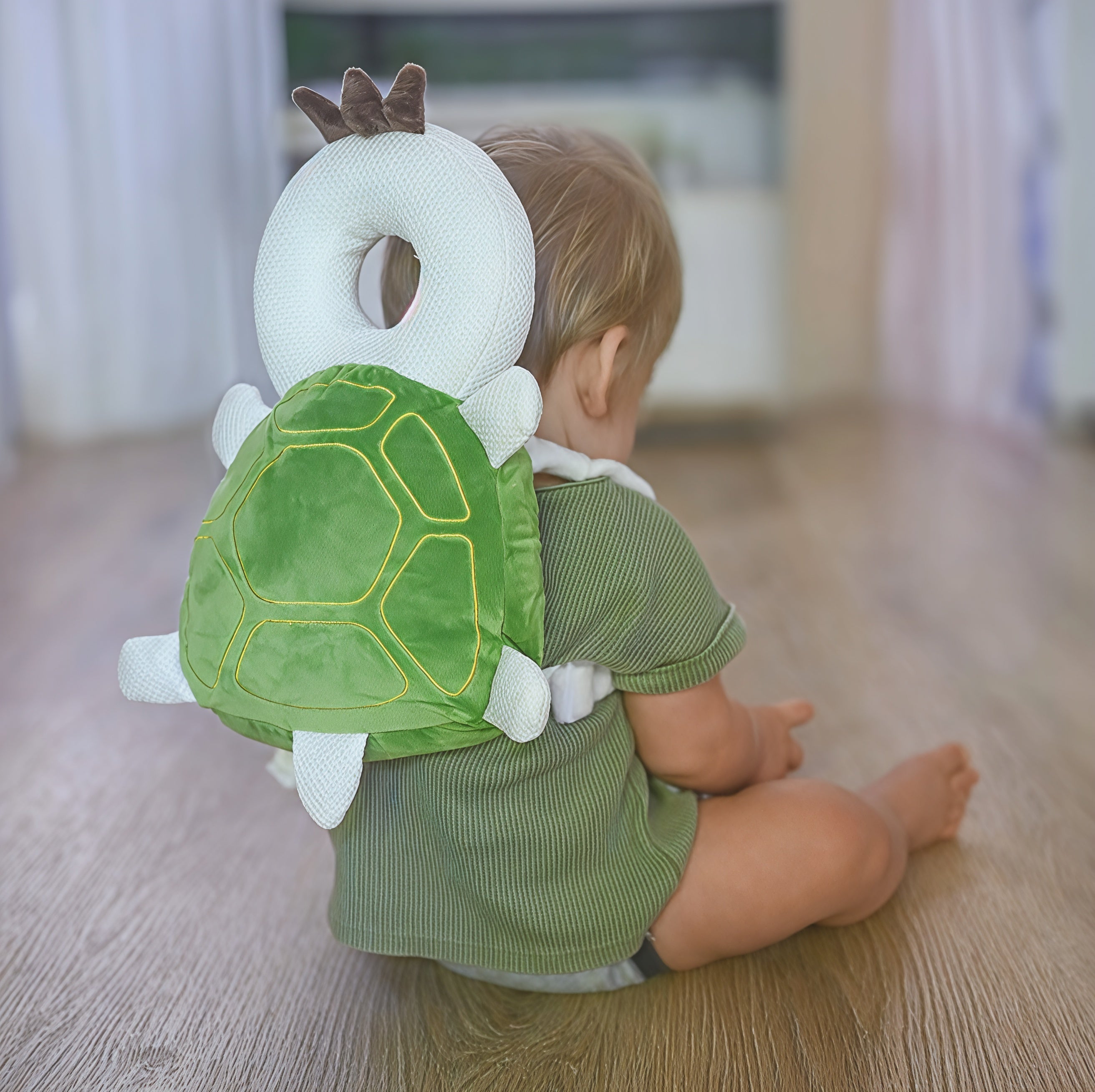 Bébé assis sur le sol portant un coussin de protection en forme de tortue. Accessoire sécurité enfant, protection tête, design mignon.