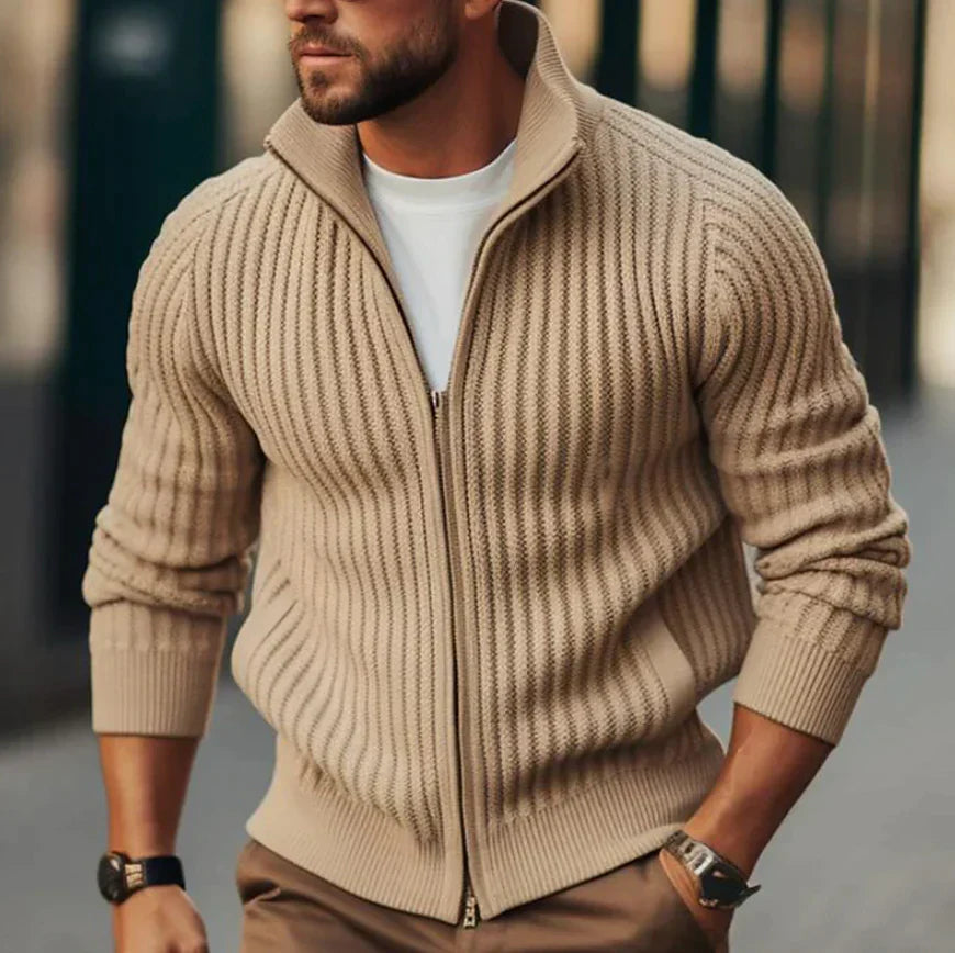 Homme portant un pull zippé beige en maille côtelée, style décontracté, mode masculine automne-hiver, rue urbaine floue en arrière-plan.