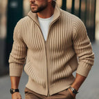 Homme portant un pull zippé beige en maille côtelée, style décontracté, mode masculine automne-hiver, rue urbaine floue en arrière-plan.