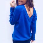 Femme souriante portant un pull bleu vif avec un dos en V, style décontracté, mode automne-hiver, tendance féminine, fond blanc.