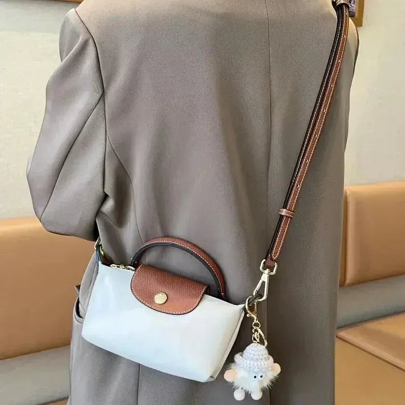 Sac à main en cuir blanc avec bandoulière marron, porté par une personne en manteau beige. Porte-clés peluche attaché. Accessoire mode élégant.