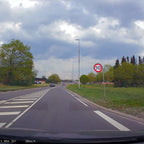 Route de campagne avec panneau de limitation de vitesse à 70 km/h, ciel nuageux, arbres verts, et voitures en circulation. Paysage printanier.