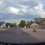 Route de campagne avec ciel nuageux, maisons résidentielles, lampadaire et gros rocher sur le trottoir. Paysage rural, journée nuageuse.