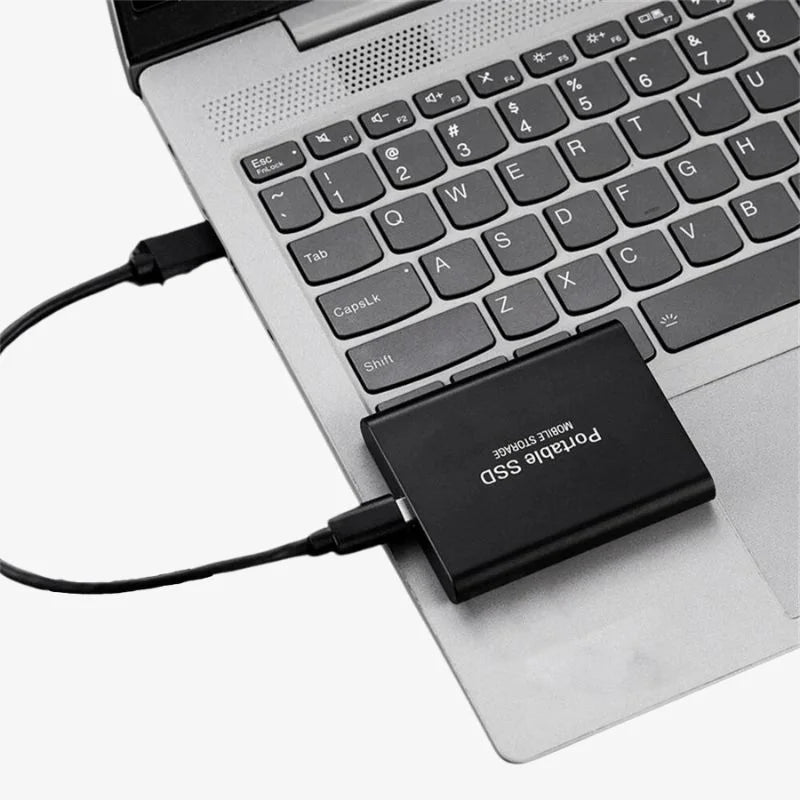 Ordinateur portable avec SSD externe connecté via USB, stockage portable, clavier argenté, technologie moderne, transfert de données rapide.