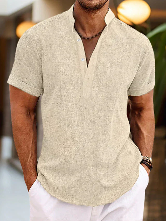 Homme portant une chemise en lin beige à manches courtes, col mao, avec un collier en perles, dans un cadre intérieur moderne.
