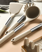 Ustensiles de cuisine modernes en silicone beige avec manches en acier inoxydable, comprenant une louche, une spatule et une cuillère à spaghetti.