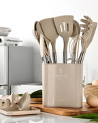 Set d'ustensiles de cuisine beige en silicone avec support, comprenant spatules, fouet et cuillère à pâtes, sur un plan de travail moderne.