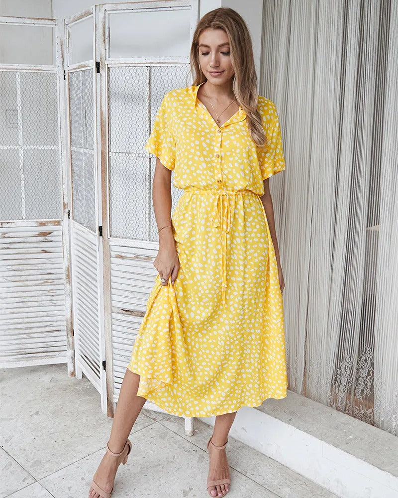 Robe d'été jaune à pois blancs, manches courtes, col chemise, portée par une femme souriante. Mode féminine, tenue estivale élégante.