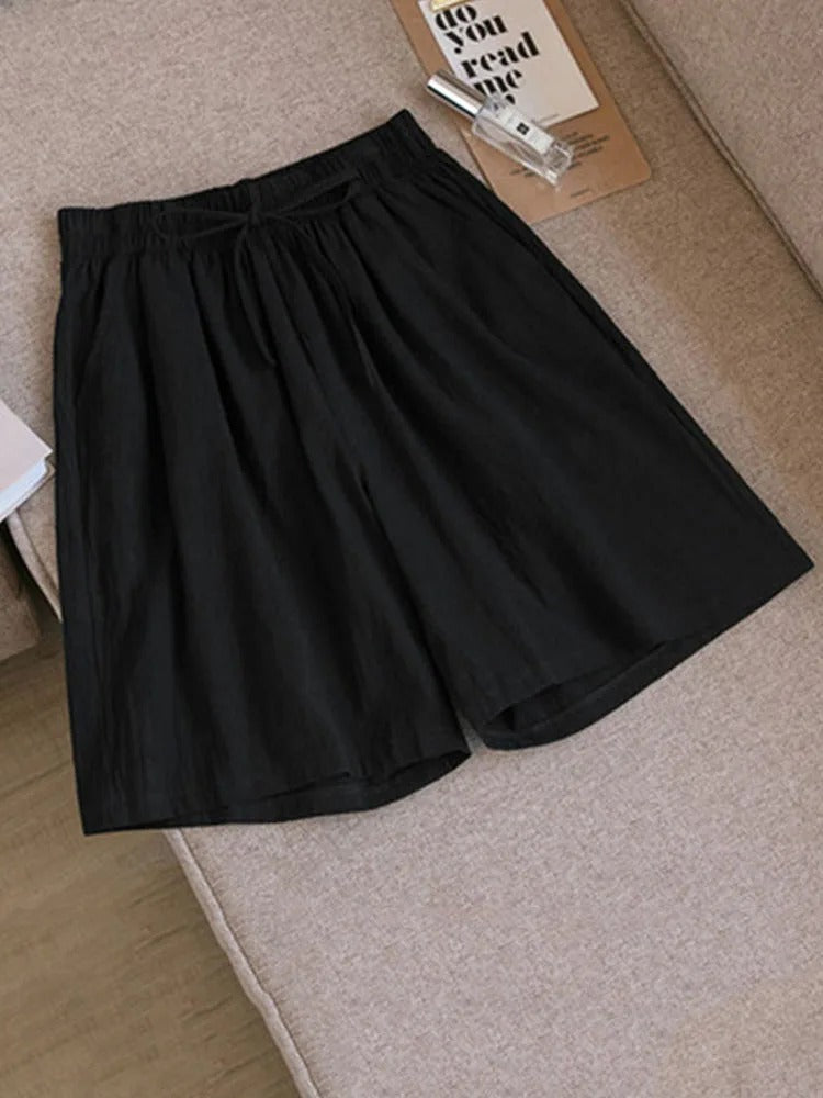 Short noir en tissu léger posé sur un canapé beige, avec un magazine et des lunettes à proximité. Mode décontractée, vêtements d'été confortables.