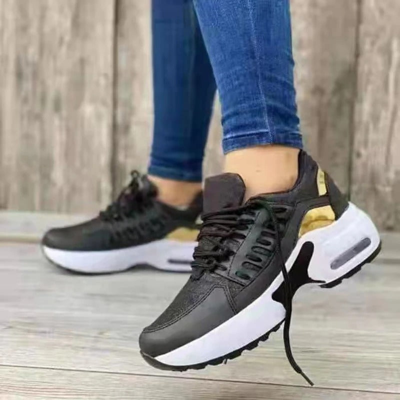 Baskets noires et blanches modernes avec détails dorés, portées avec un jean bleu, posées sur un sol en bois. Mode, chaussures tendance, style urbain.