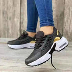 Baskets noires et blanches modernes avec détails dorés, portées avec un jean bleu, posées sur un sol en bois. Mode, chaussures tendance, style urbain.
