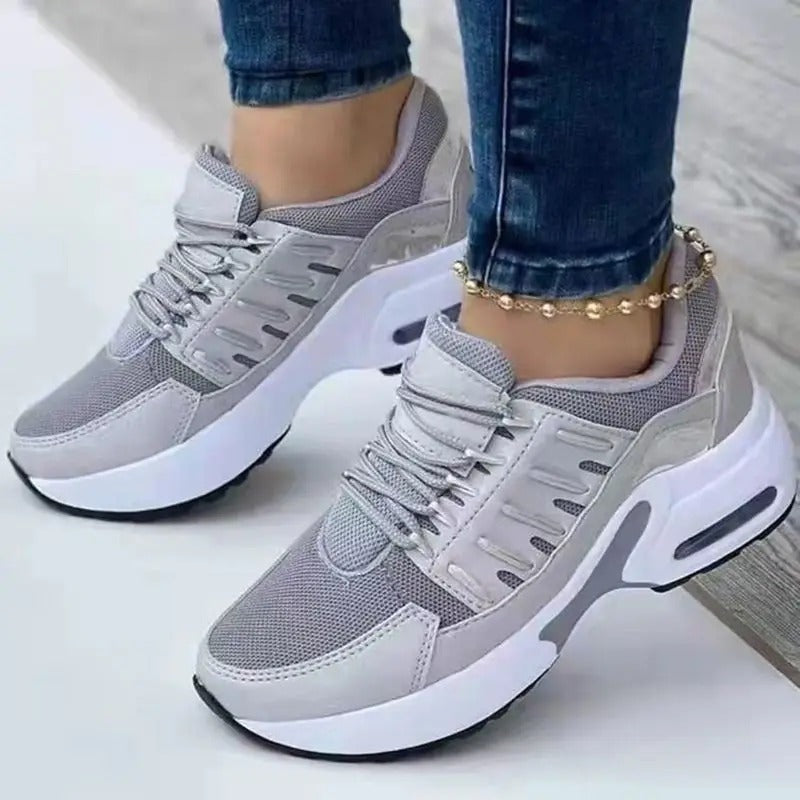Chaussures de sport grises pour femme, design moderne avec semelle épaisse blanche, portées avec un jean et un bracelet de cheville doré.