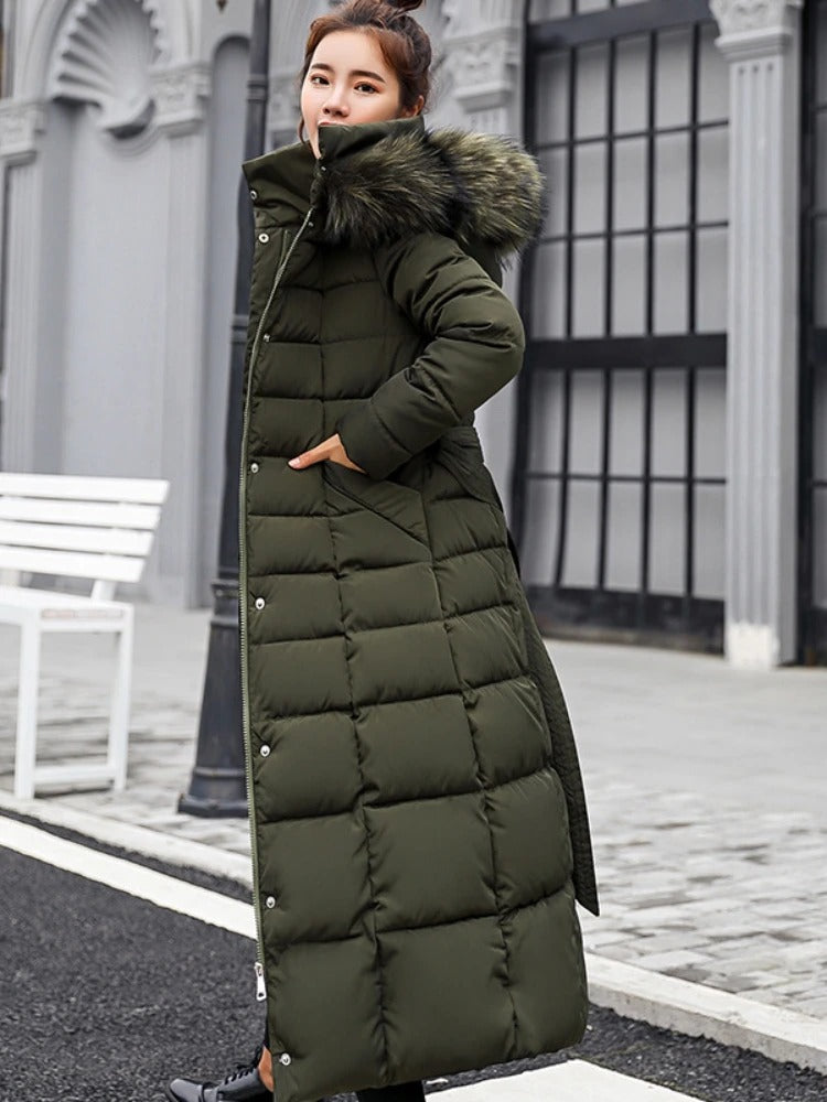 Femme portant un long manteau d'hiver matelassé vert avec capuche en fausse fourrure, debout dans une rue urbaine. Mode hiver, manteau chaud.
