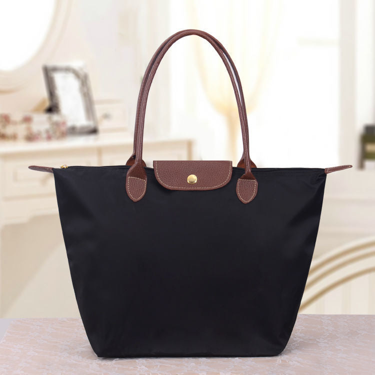 Sac à main noir élégant avec poignées marron en cuir, posé sur une table. Accessoire mode femme, design classique, idéal pour le quotidien.
