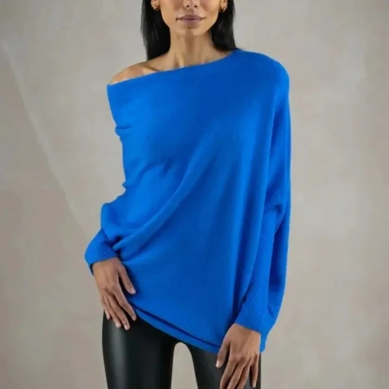 Femme portant un pull bleu oversize asymétrique, manches longues, avec leggings noirs. Mode décontractée, tendance automne-hiver.