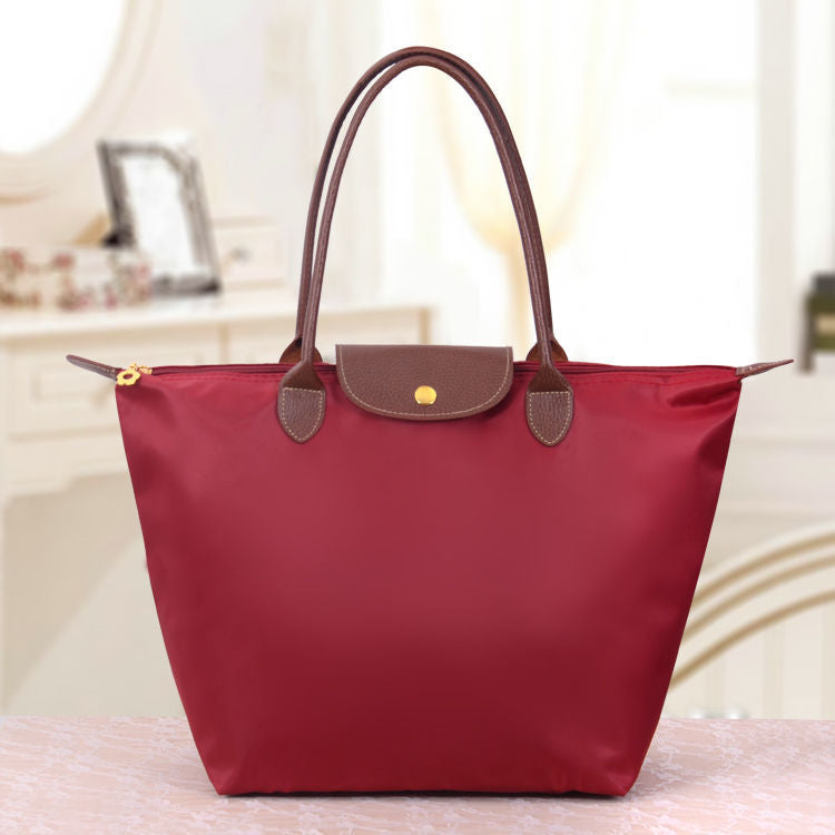 Sac à main rouge élégant avec poignées marron, posé sur une table. Design moderne et chic, idéal pour la mode féminine. Accessoire tendance.