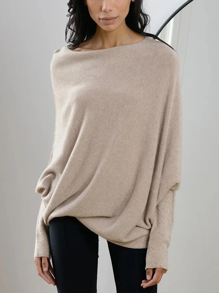 Femme portant un pull beige ample en laine, manches longues, col bateau, associé à un pantalon noir. Mode automne-hiver élégante et confortable.