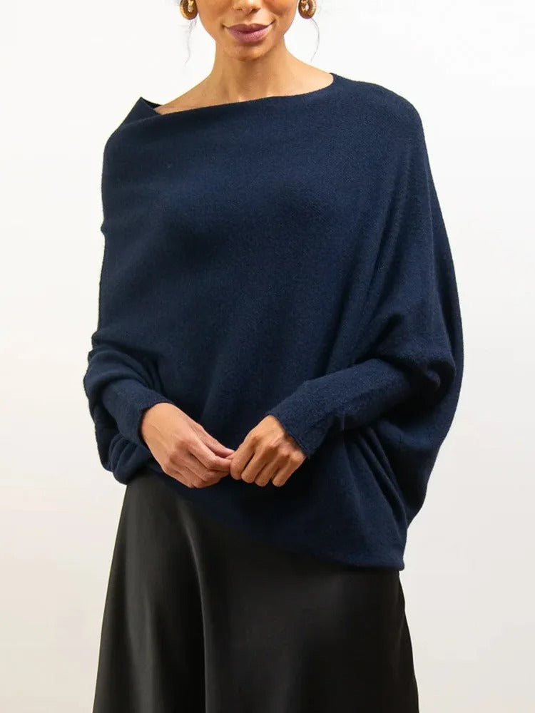Femme portant un pull bleu marine ample en cachemire, manches longues, col bateau, jupe noire. Mode élégante, tenue automne-hiver chic.