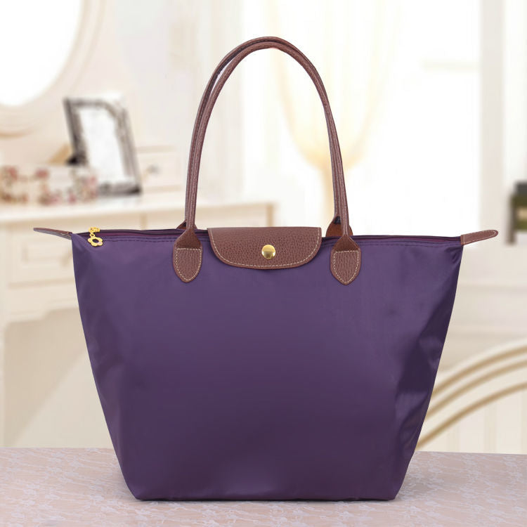 Sac à main violet élégant avec poignées marron, posé sur une table. Accessoire de mode chic, idéal pour un style moderne et raffiné.