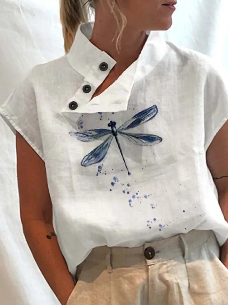 Femme portant une chemise blanche en lin avec motif libellule bleue, col boutonné, manches courtes. Mode éco-responsable, style décontracté.