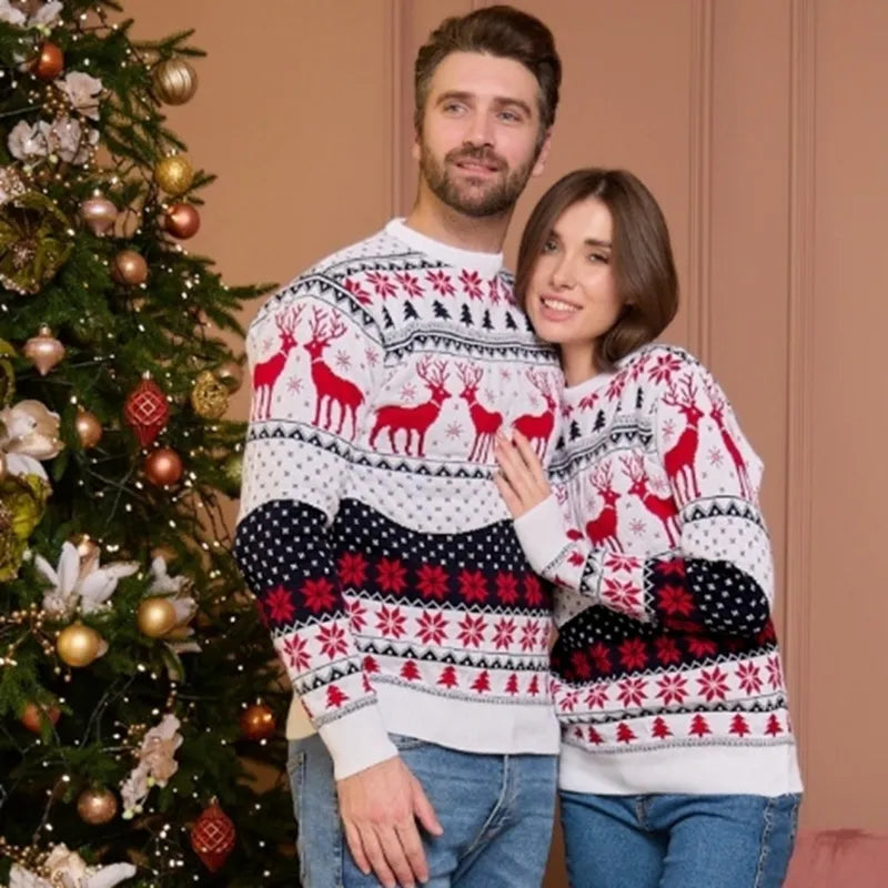 Couple portant des pulls de Noël assortis avec motifs de rennes rouges, posant devant un sapin décoré. Mode festive, tenues de Noël tendance.