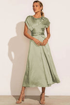 Robe longue verte élégante en satin, manches courtes, ceinture drapée, portée par une femme. Mode féminine chic, tenue de soirée tendance.
