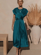 Robe longue bleu sarcelle élégante portée par une femme, avec un vase décoratif en arrière-plan. Mode féminine chic, tenue estivale tendance.