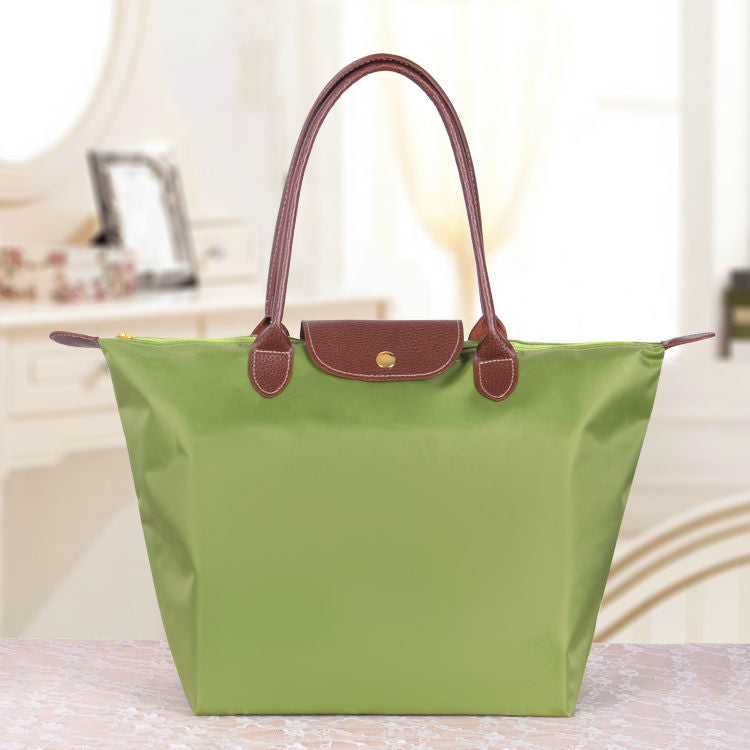 Sac à main vert en toile avec poignées en cuir marron, posé sur une table. Accessoire de mode élégant pour femme, idéal pour le quotidien.