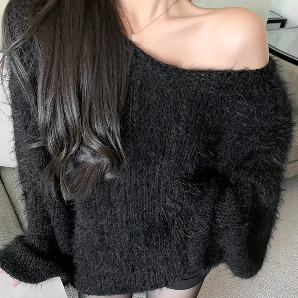 Femme portant un pull noir en laine duveteuse, épaule dénudée, cheveux longs et bruns. Mode automne-hiver, style décontracté et élégant.