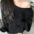 Femme portant un pull noir en laine duveteuse, épaule dénudée, cheveux longs et bruns. Mode automne-hiver, style décontracté et élégant.